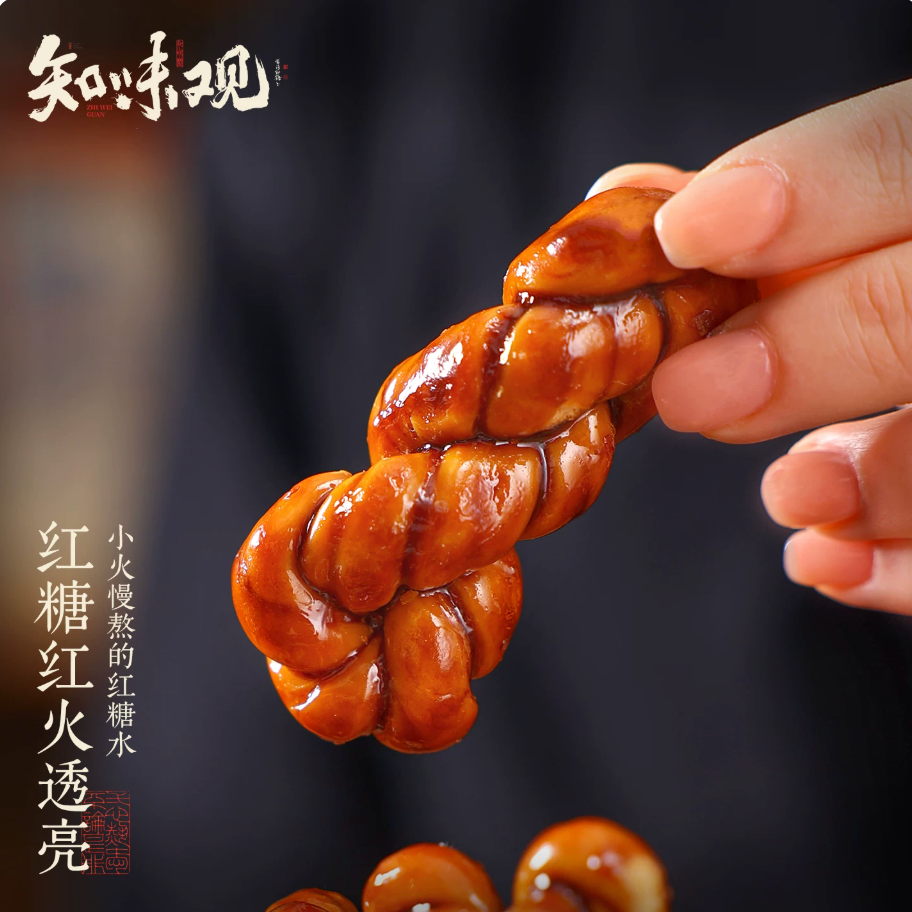 Hand holding a single Zhiweiguan brown sugar mahua twist — slow-cooked brown sugar glaze, golden and glossy