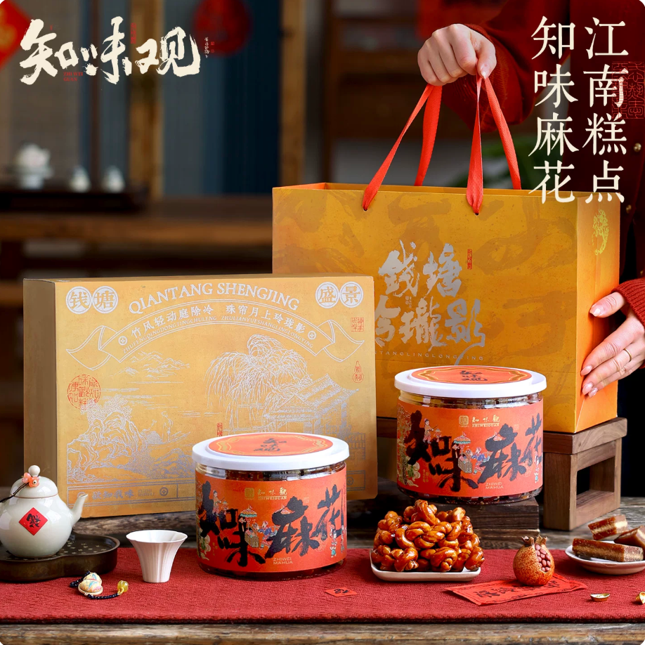Zhiweiguan Brown Sugar Mahua gift box with golden gift bag, two orange tins and mahua pieces displayed on festive red table setting
