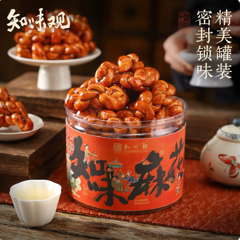 A pile of glossy, amber-colored brown sugar mahua twists stacked on a porcelain stand next to a traditional Chinese tea cup.