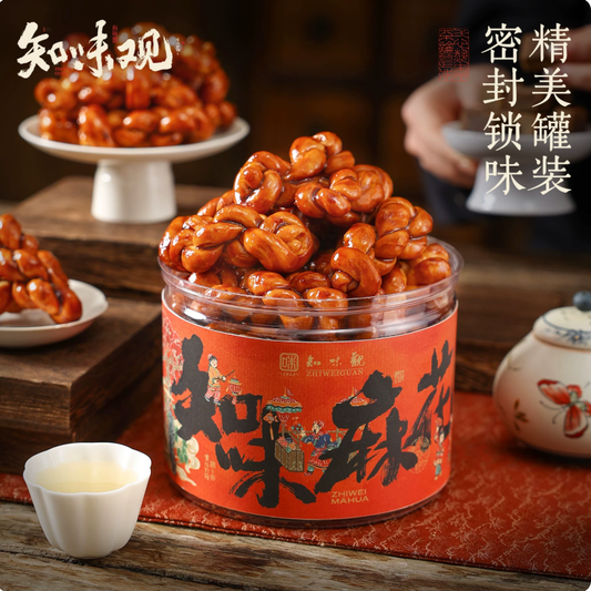 A pile of glossy, amber-colored brown sugar mahua twists stacked on a porcelain stand next to a traditional Chinese tea cup.